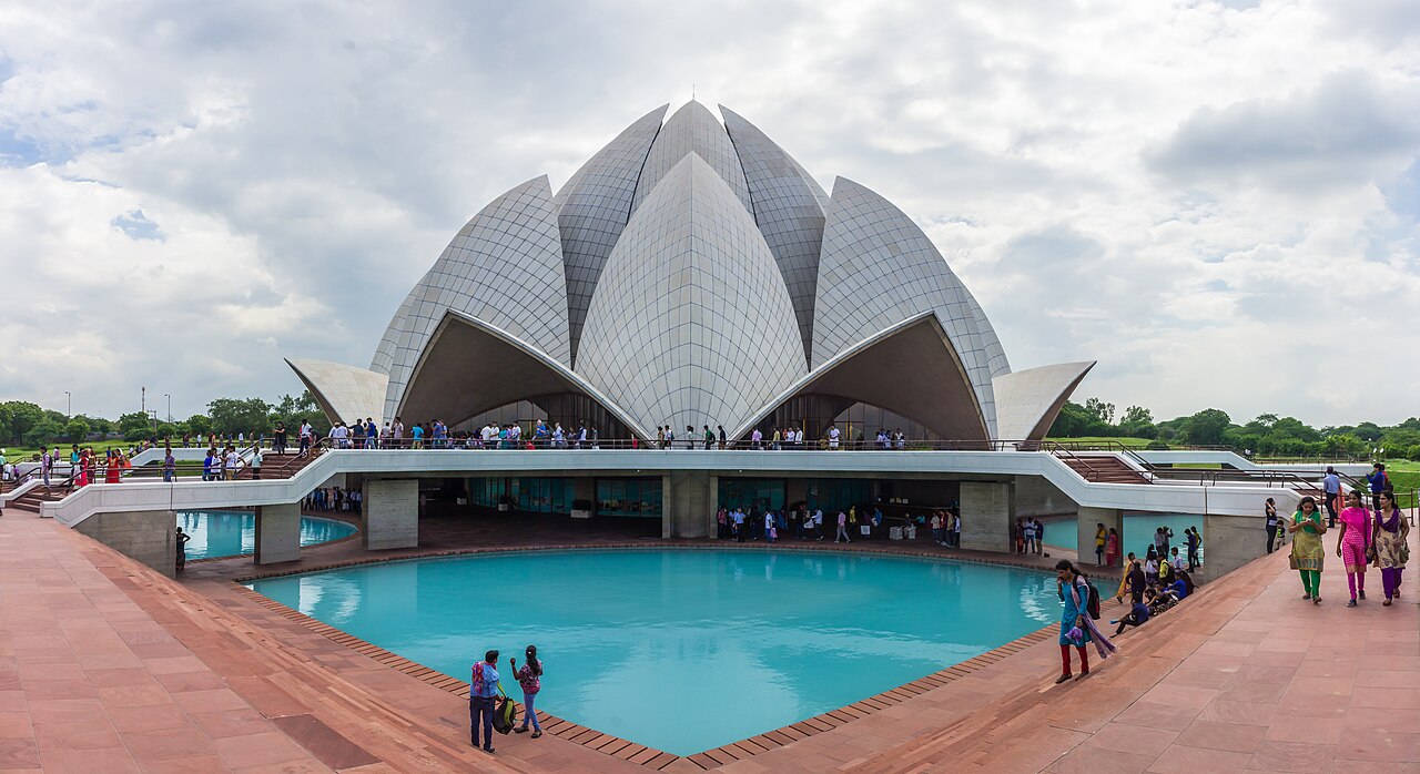 The white marble Lotus Temple in Delhi, its petal-shaped shells rising over a turquoise pool, with visitors on the terraces.