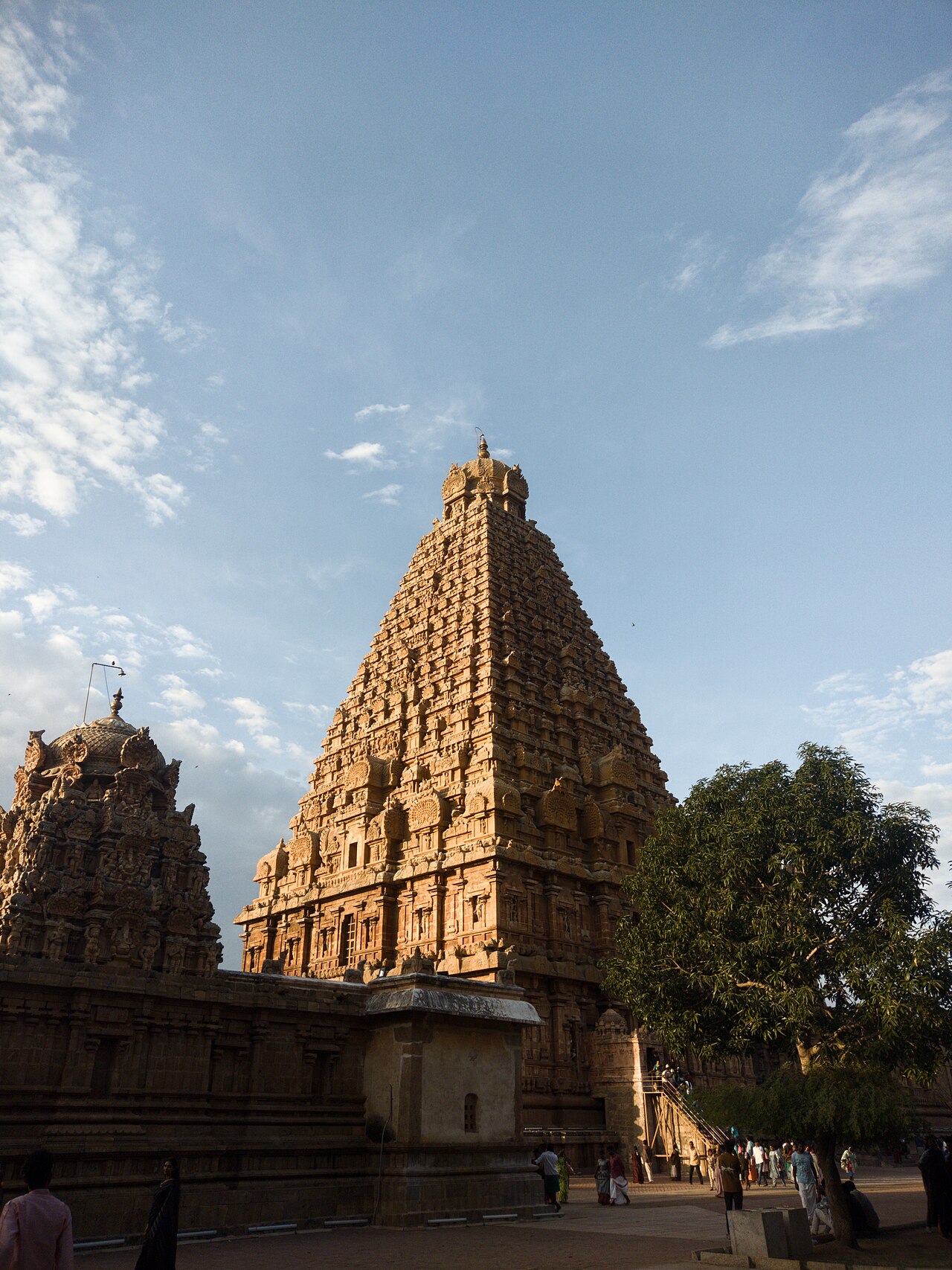 The towering granite vimana of the Brihadeeswara Temple at Thanjavur, its sculpted tiers catching late-afternoon light, visitors in the courtyard below.