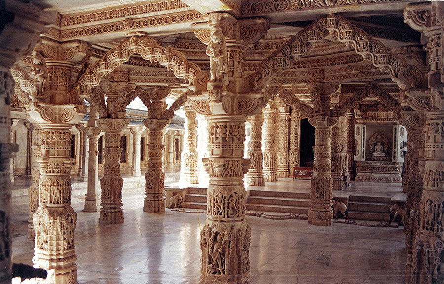 The marble interior of the Luna Vasahi temple at Dilwara: densely carved pillars and arches, a small Tirthankara shrine visible at the rear.