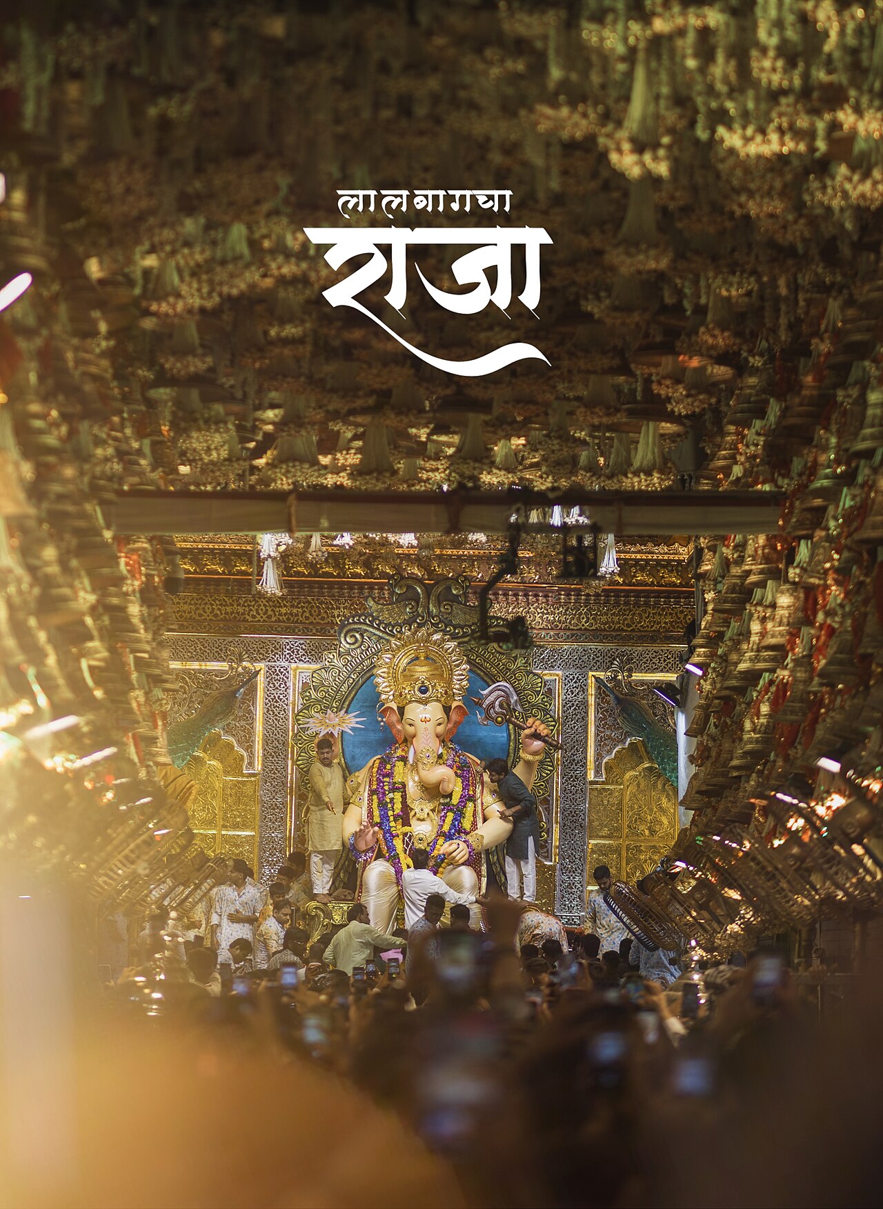 A colossal seated Ganesh idol crowned and garlanded on a golden pandal throne, devotees crowding forward with phones raised during the Mumbai festival.