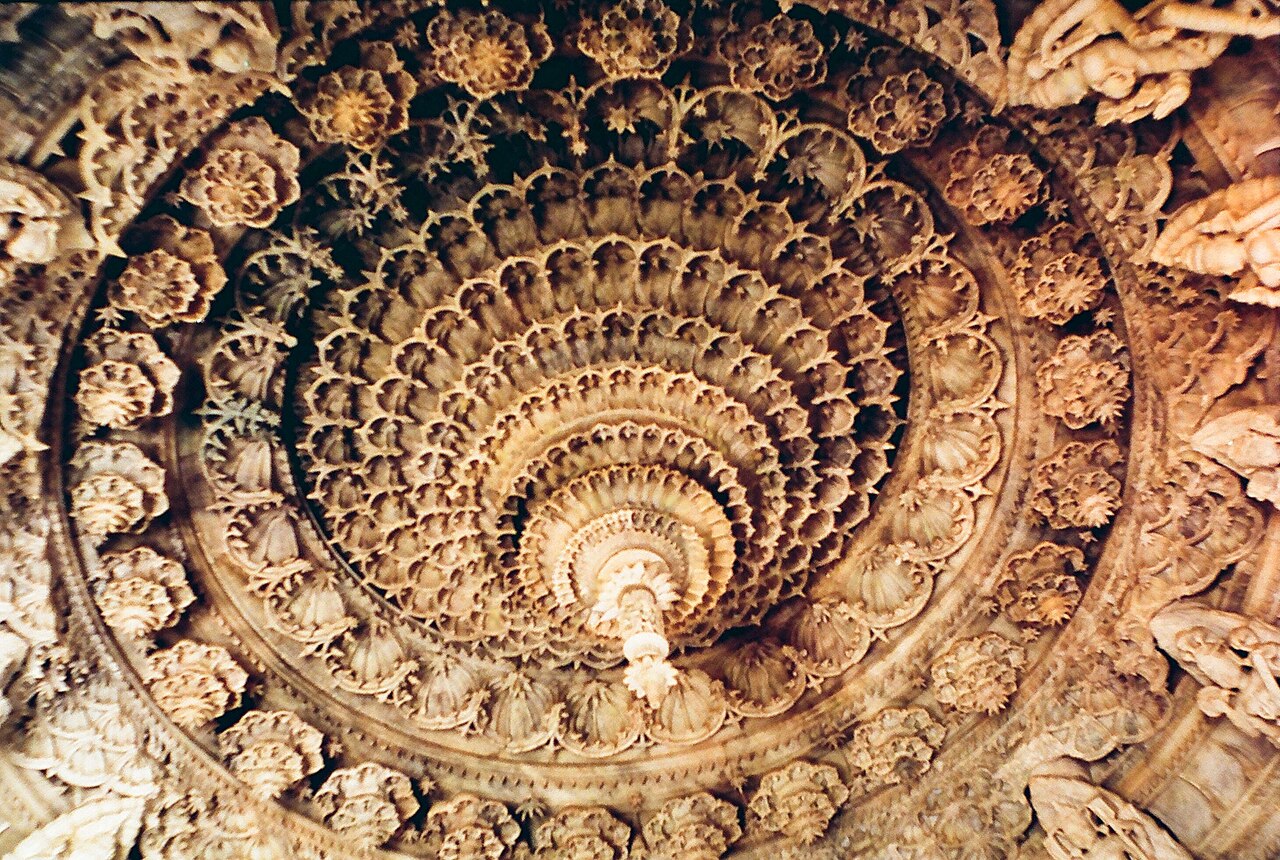 Looking straight up into the concentric carved marble dome ceiling of a Dilwara temple, ring upon ring of scalloped stone petals and figures.