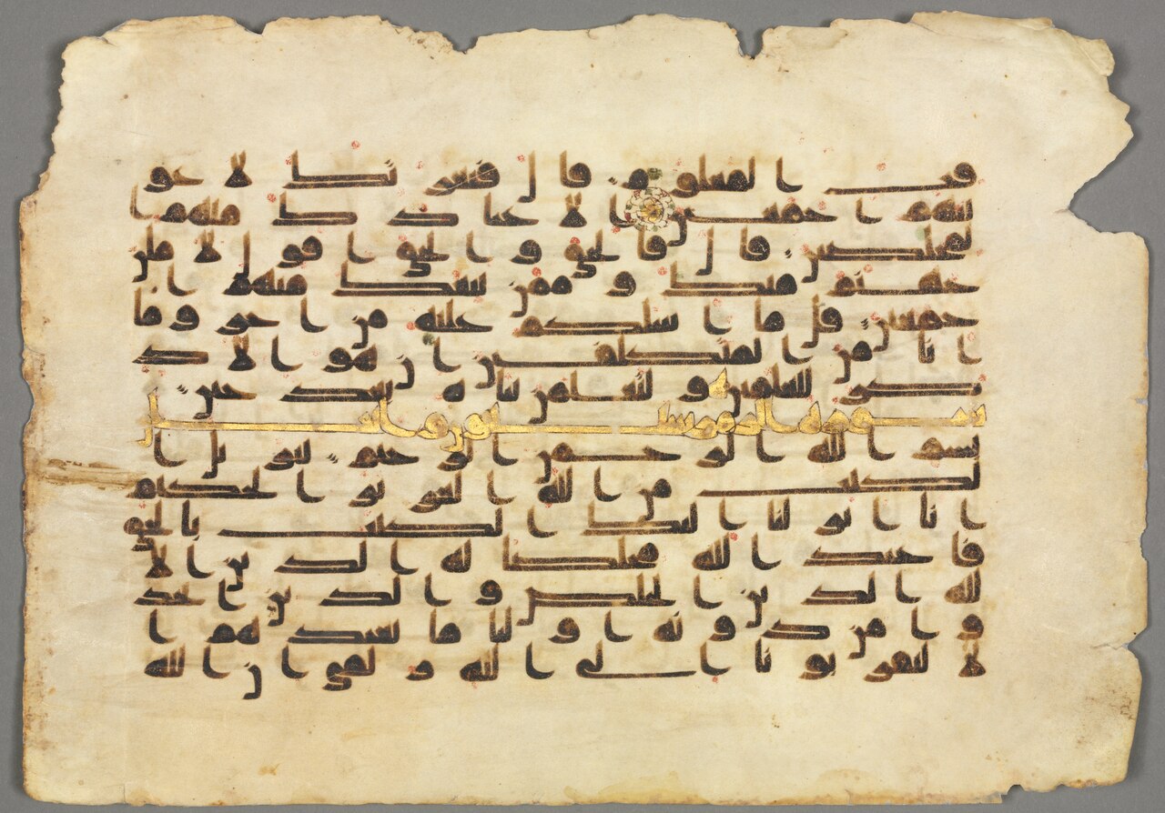 A parchment folio of an Abbasid Qur'an written in bold angular Kufic script, with a gold verse marker and red vocalization dots.