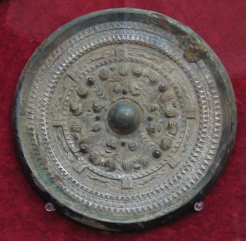 The decorated back of a Kofun-period bronze mirror, cast with deities and beasts in concentric bands around a central boss.