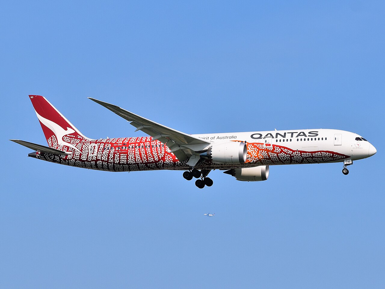 A Qantas Boeing 787-9 in flight, its fuselage wrapped in the red, ochre, and white dot-work of the livery adapted from Emily Kame Kngwarreye's painting Yam Dreaming.