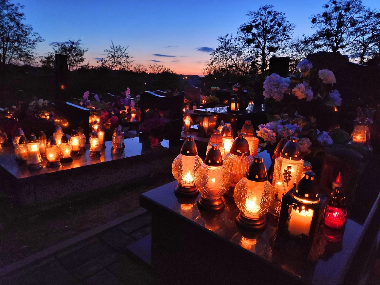 Graves covered with lit candles in a Polish cemetery at dusk.