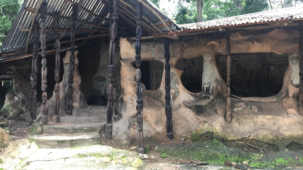 A sculpted mud-and-timber shrine building stands among trees in the Osun-Osogbo Sacred Grove in Nigeria.