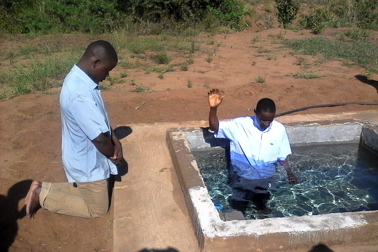 A believer being baptized by immersion in an outdoor pool in Mozambique, the baptizer kneeling beside him.
