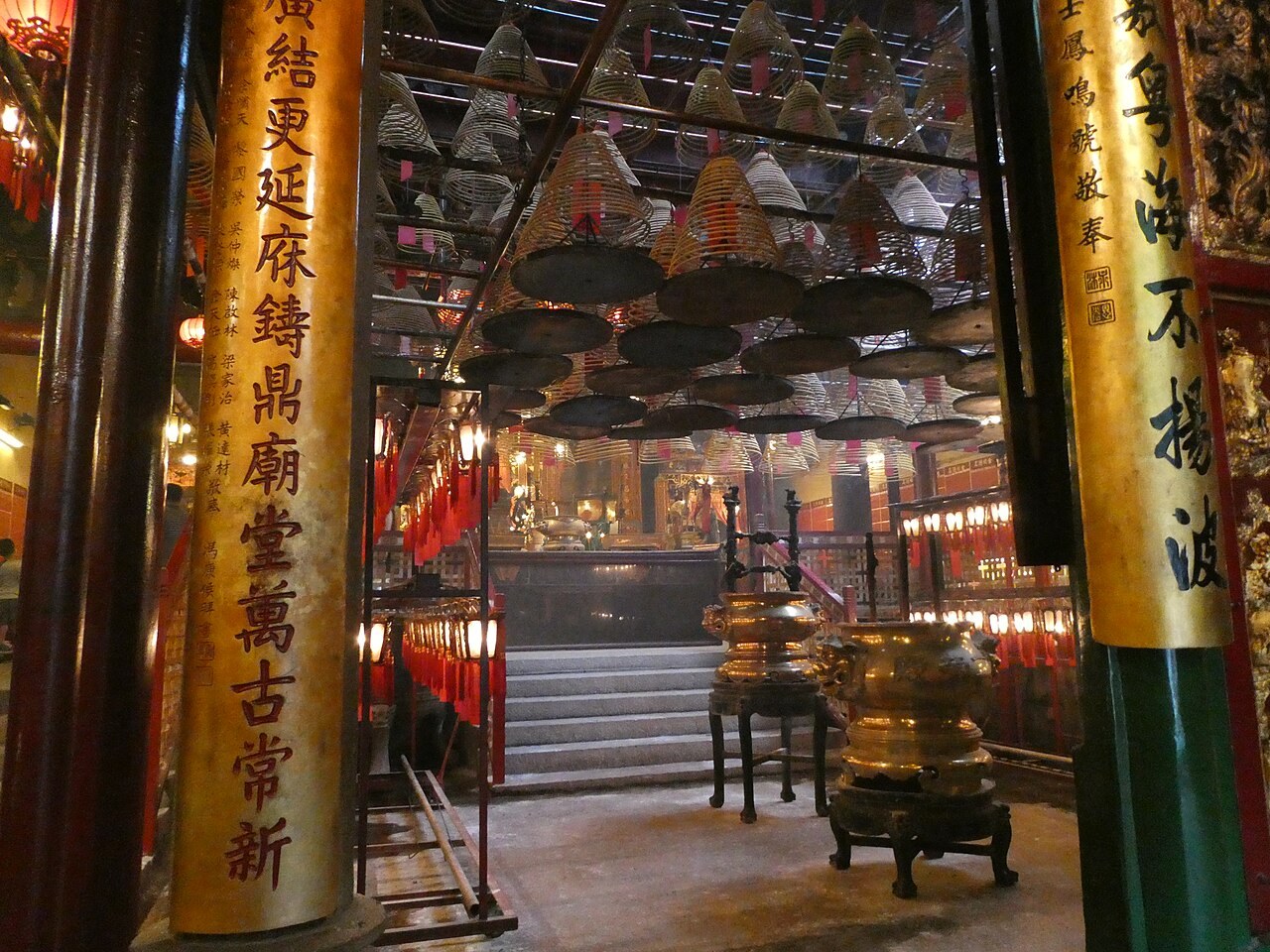 Inside Hong Kong's Man Mo Temple, spiral incense coils hang above inscribed pillars and bronze urns.