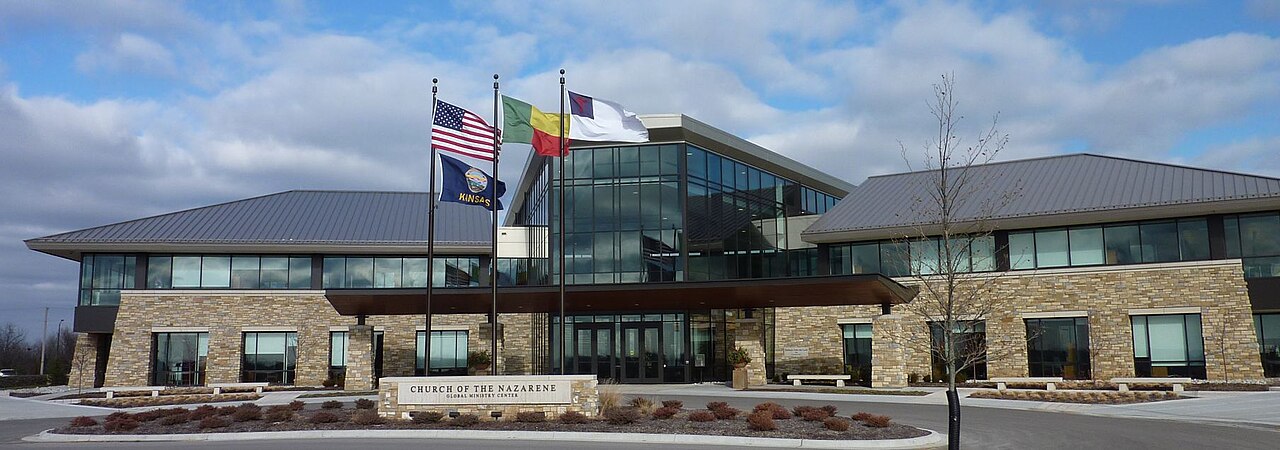 The modern stone-and-glass Global Ministry Center of the Church of the Nazarene in Lenexa, Kansas, flags flying in front.