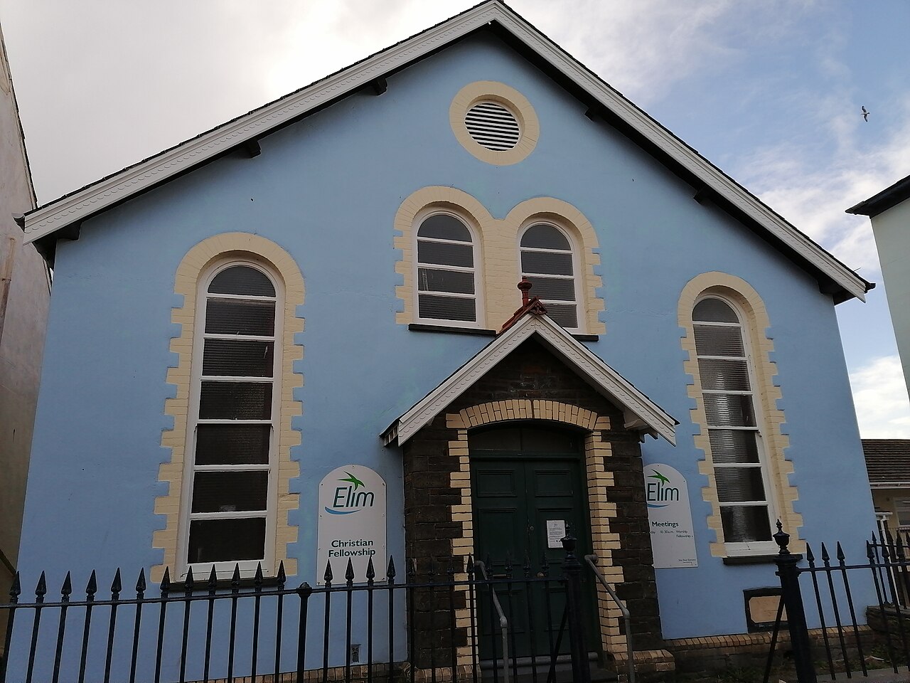 A light-blue Elim Pentecostal church with arched windows and Elim signs beside its door.