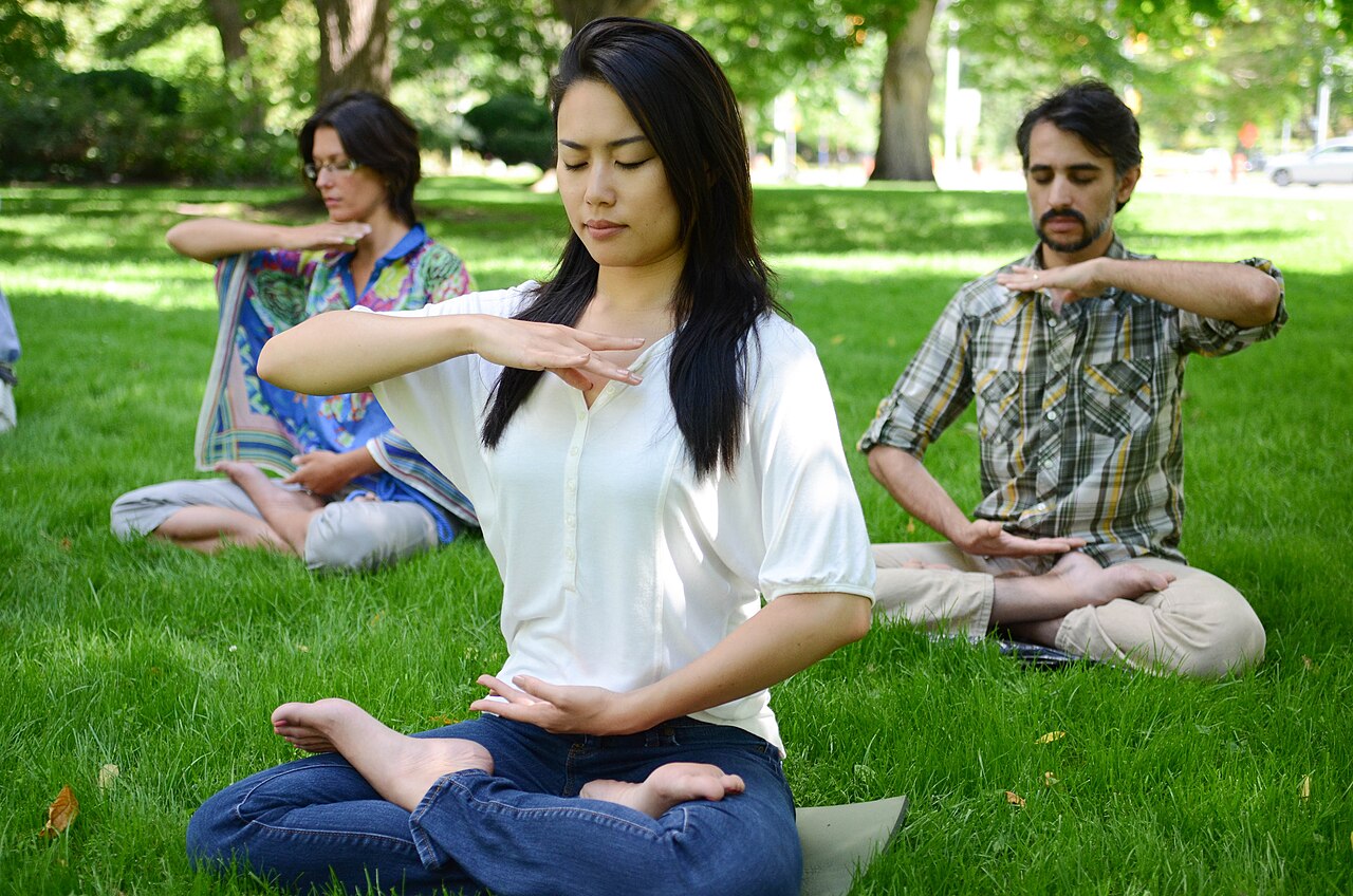 Three Falun Gong practitioners sitting cross-legged in meditation on the grass of a Toronto park.