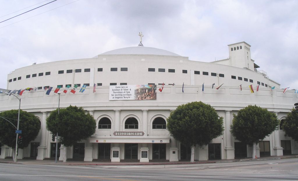 The white domed Angelus Temple in Los Angeles, flags and rounded trees along its front.