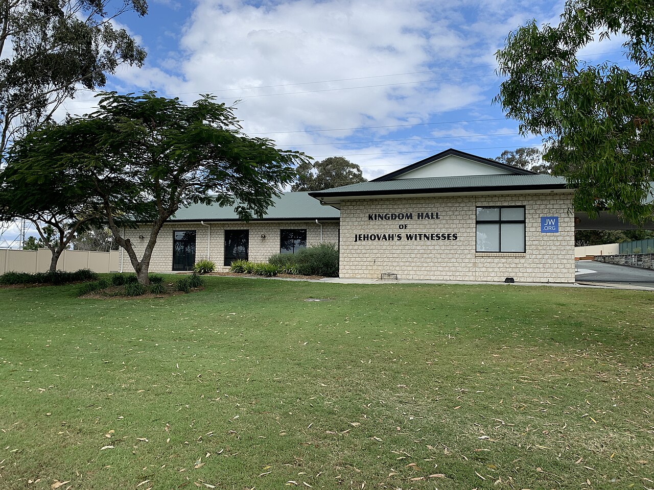 A single-story Kingdom Hall of Jehovah's Witnesses on a grassy corner in Willawong, its name on the wall.