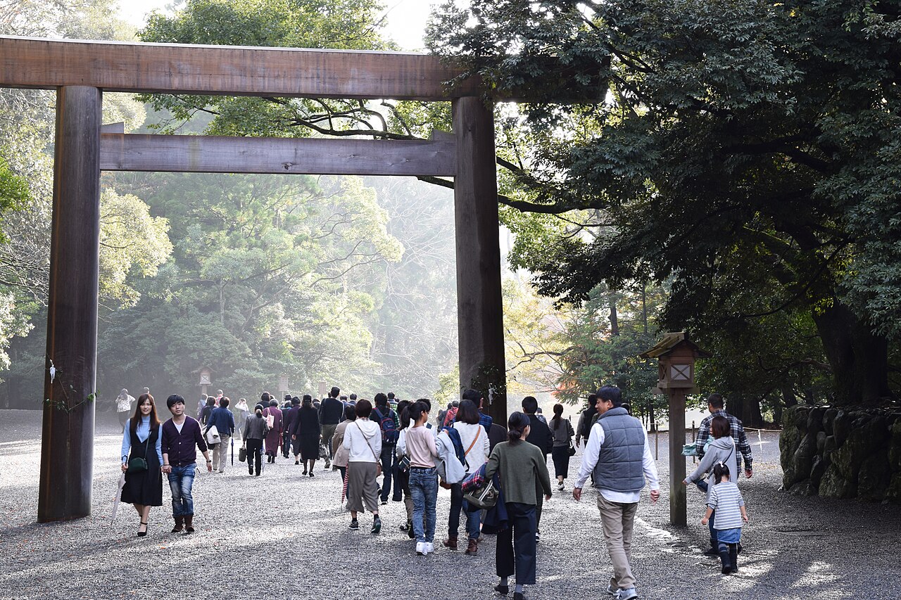 Visitors passing beneath the great wooden torii on the wooded approach to the Ise Grand Shrine in Mie, Japan.