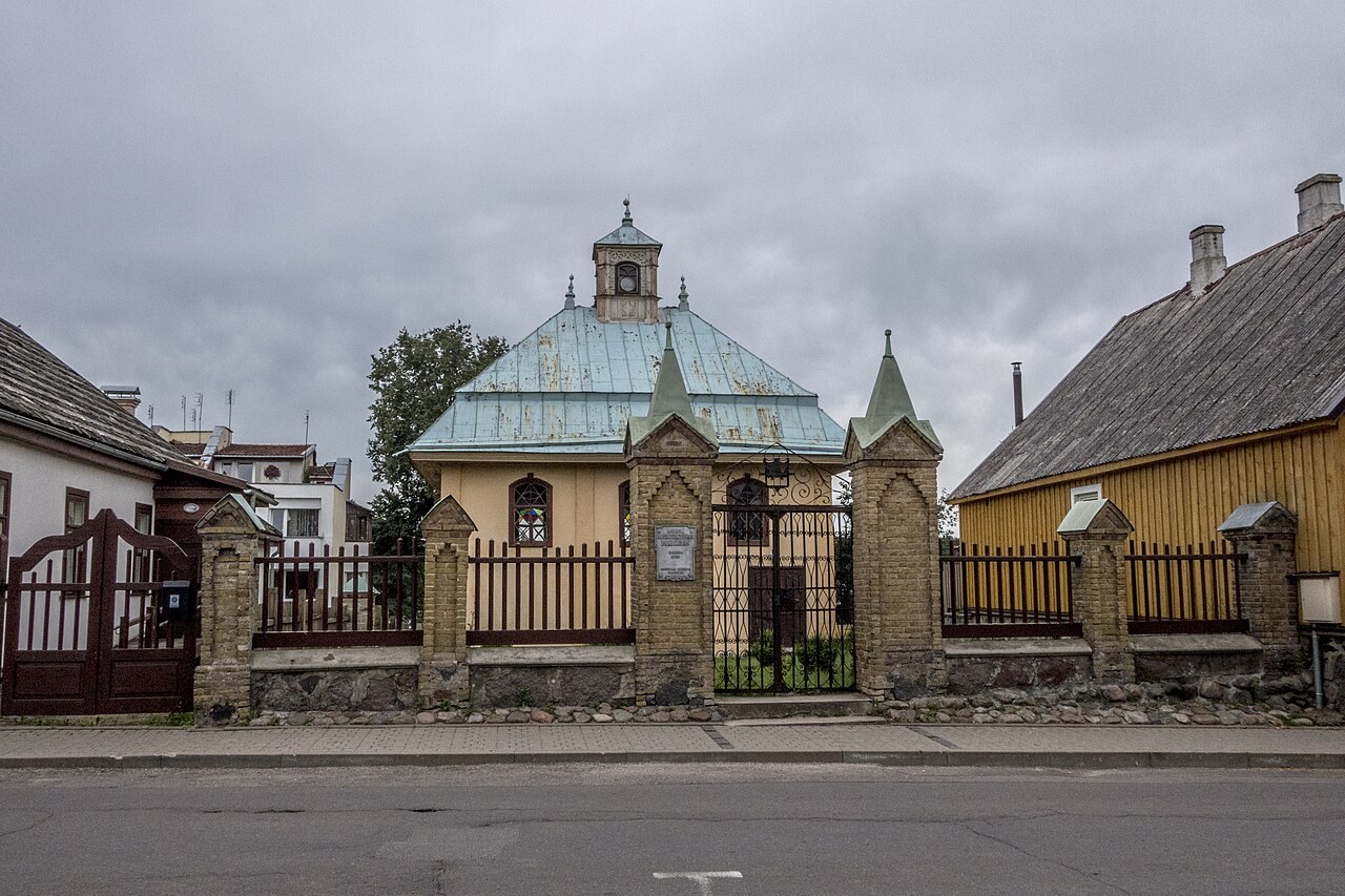 The Karaite kenesa in Trakai, Lithuania, a small pale synagogue with a green pyramidal roof, stands behind its street gate.
