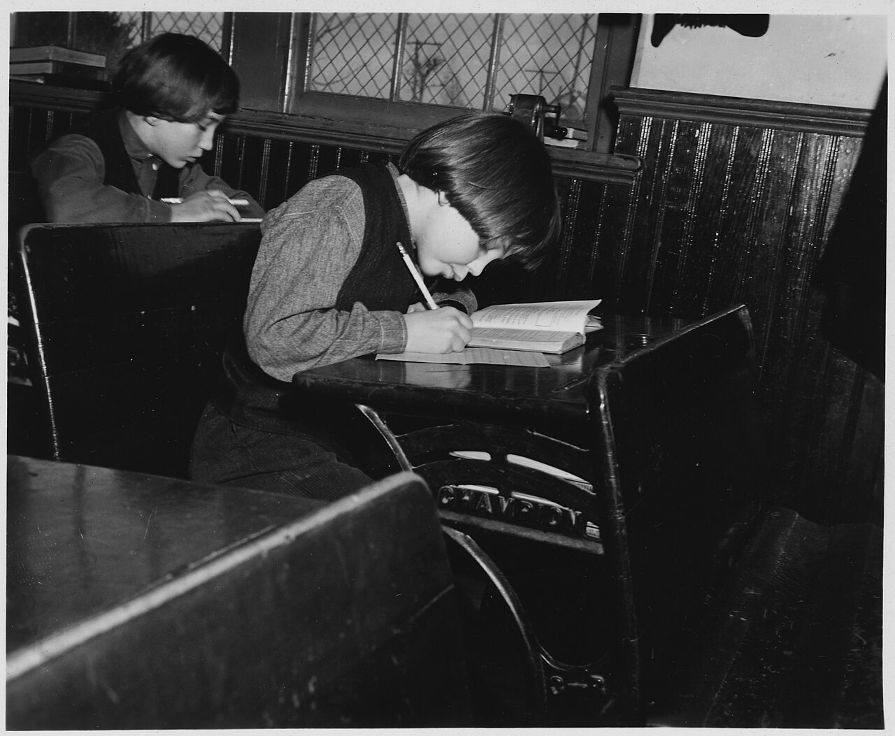 Amish schoolchildren writing at their desks in a one-room schoolhouse.