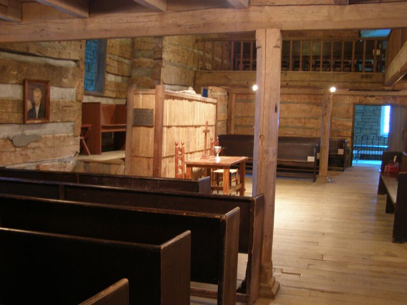 Inside the log Cane Ridge Meeting House in Kentucky, rows of wooden benches under a beamed ceiling.