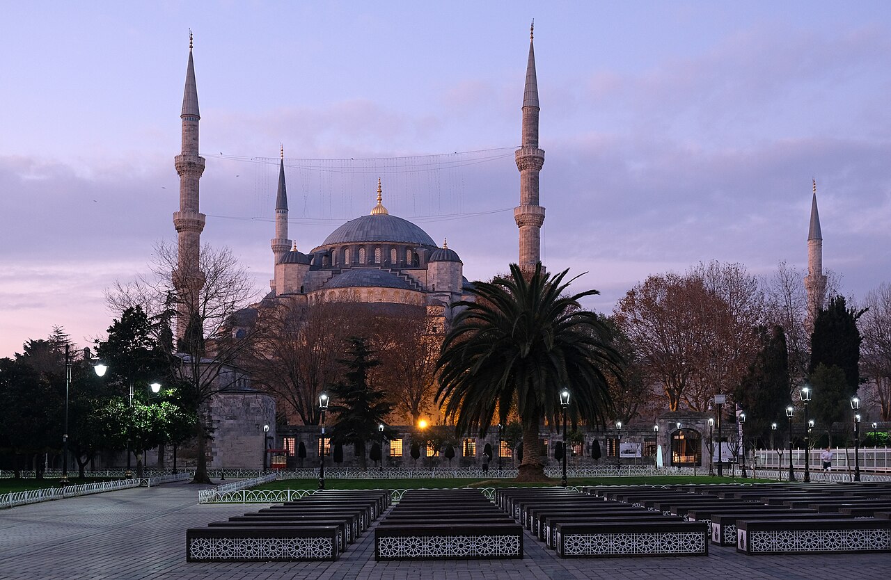 The Sultan Ahmed Mosque in Istanbul at dusk, its great dome and minarets seen across the courtyard forecourt.