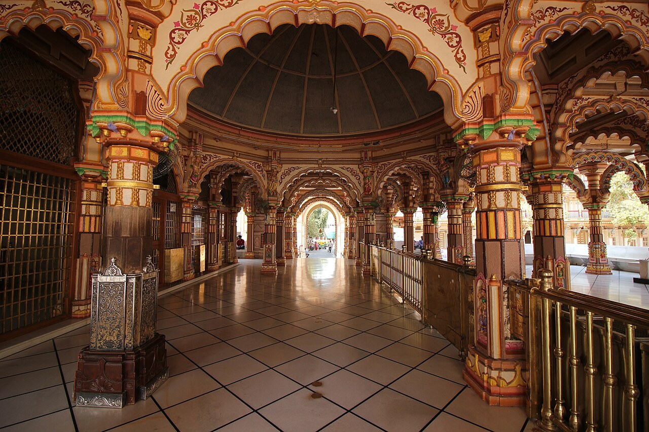 A richly painted pillared hall inside the Kalupur Swaminarayan Mandir in Ahmedabad glows with carved arches.