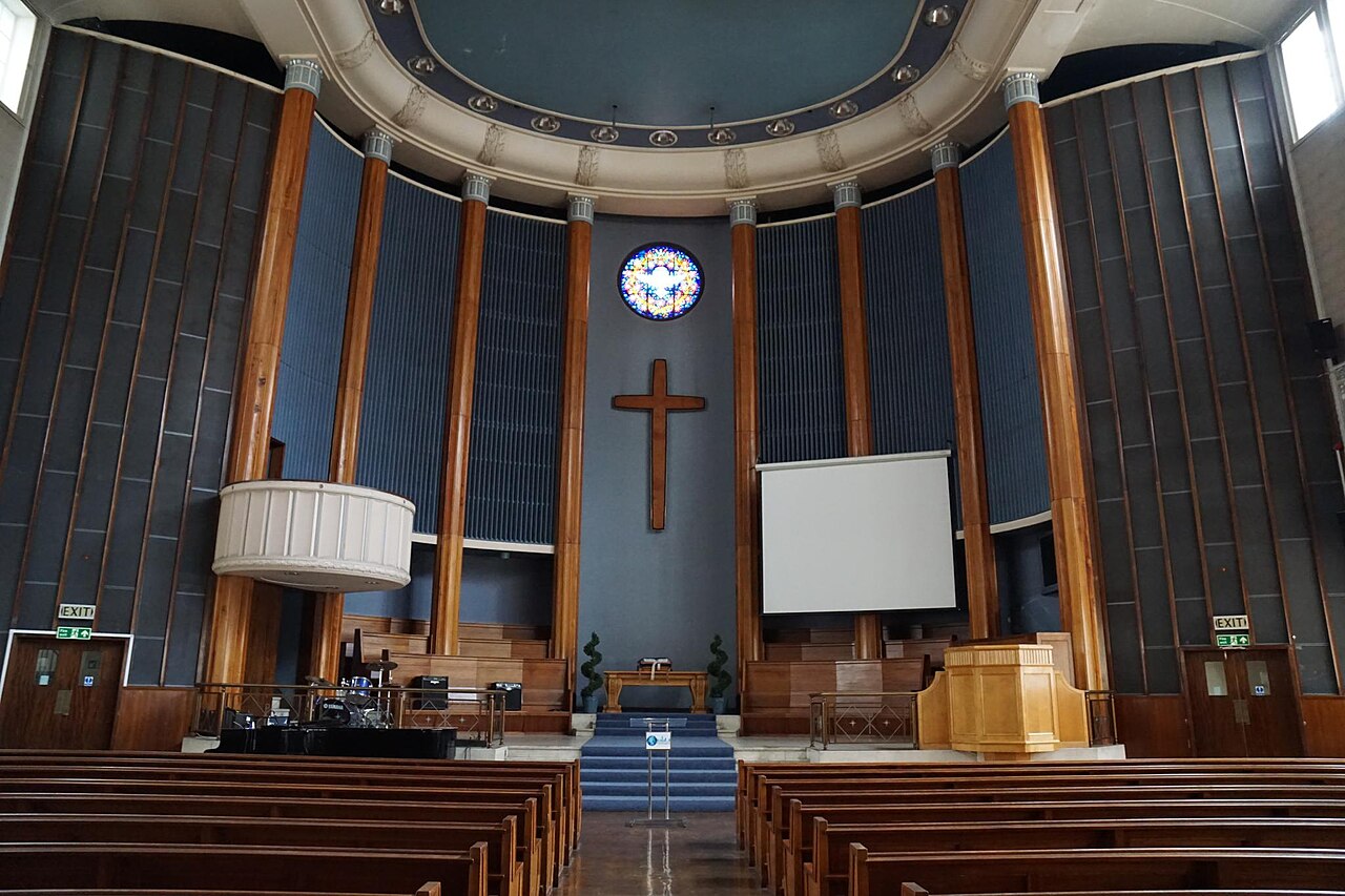 Inside London's City Temple: pews facing the domed chancel with its cross, clock, and organ pipes.