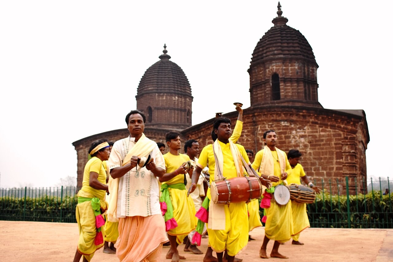 Devotees in yellow dress singing kirtan with hand cymbals and khol drums before a temple in Bishnupur.