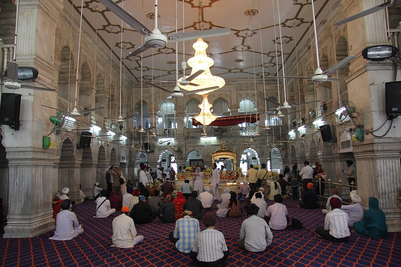 Rāgīs performing kīrtan with harmonium and tabla inside a gurdwara.