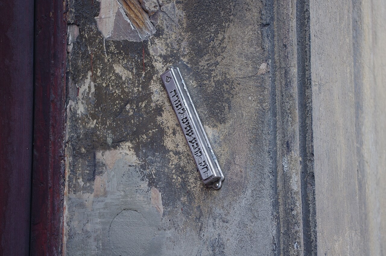 A metal mezuzah case with Hebrew lettering, fixed at an angle to a stone doorpost in Kraków.