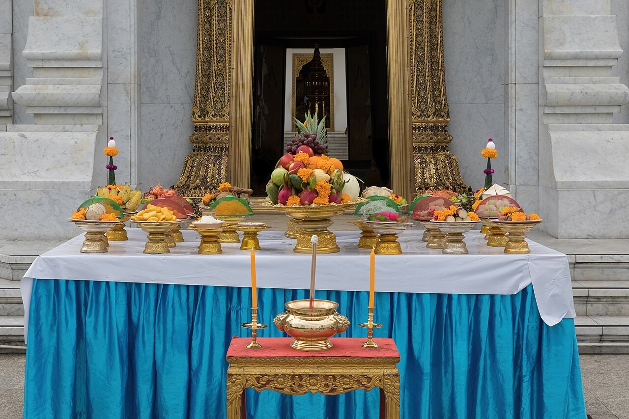 An offering table with fruit, rice, flowers, and candles at the Bangkok City Pillar Shrine.