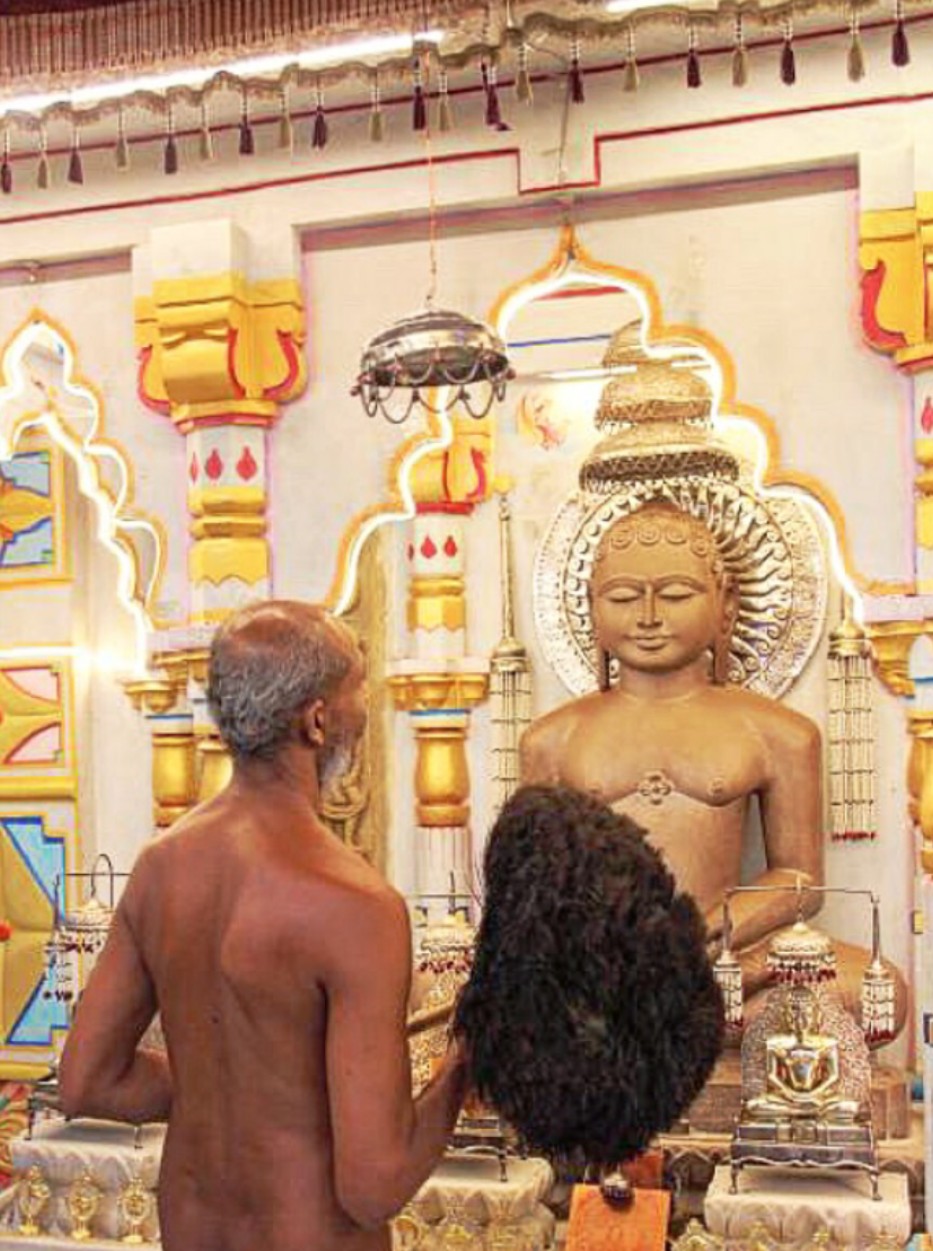 A Digambara Jain monk bowing before a Tīrthaṅkara image in a Jain temple.