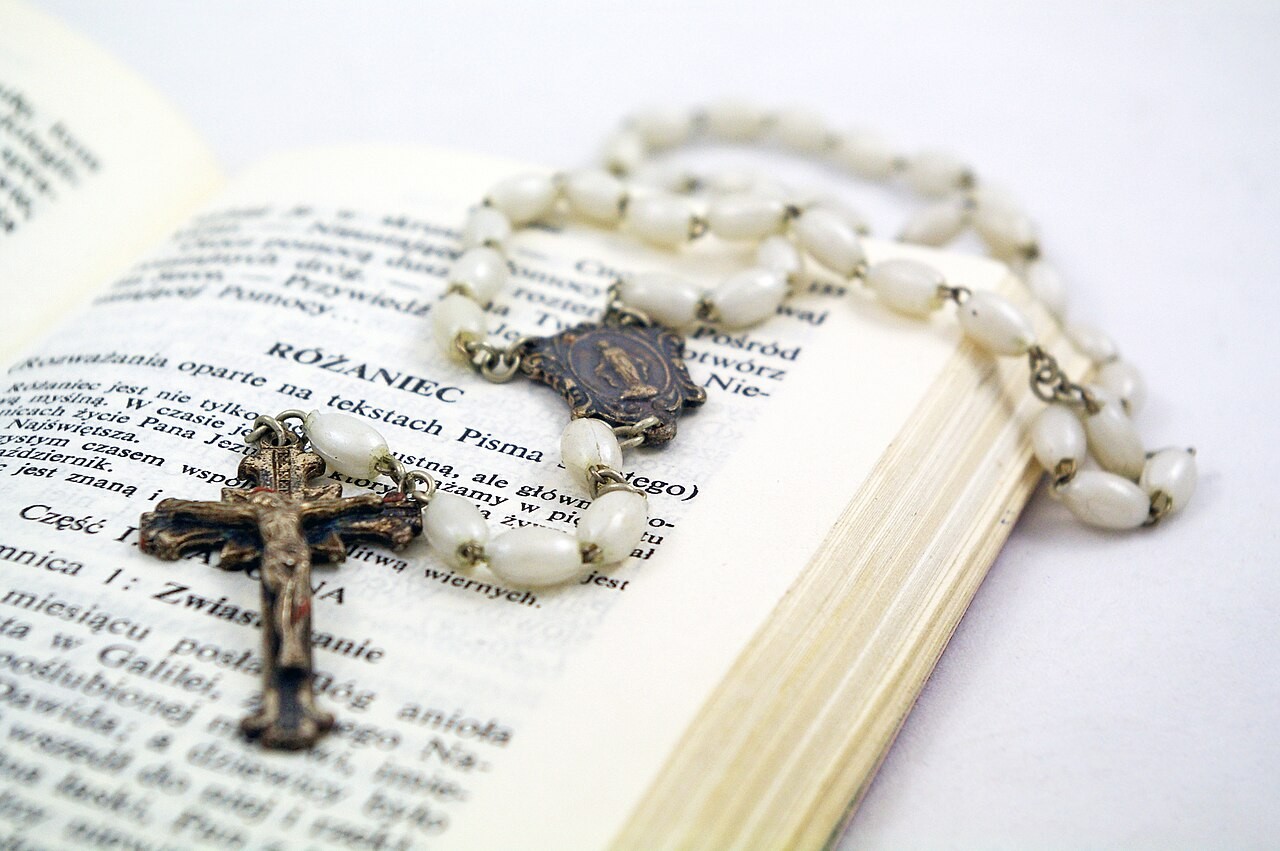 A white-beaded rosary with a crucifix and Marian medal resting on an open prayer book.