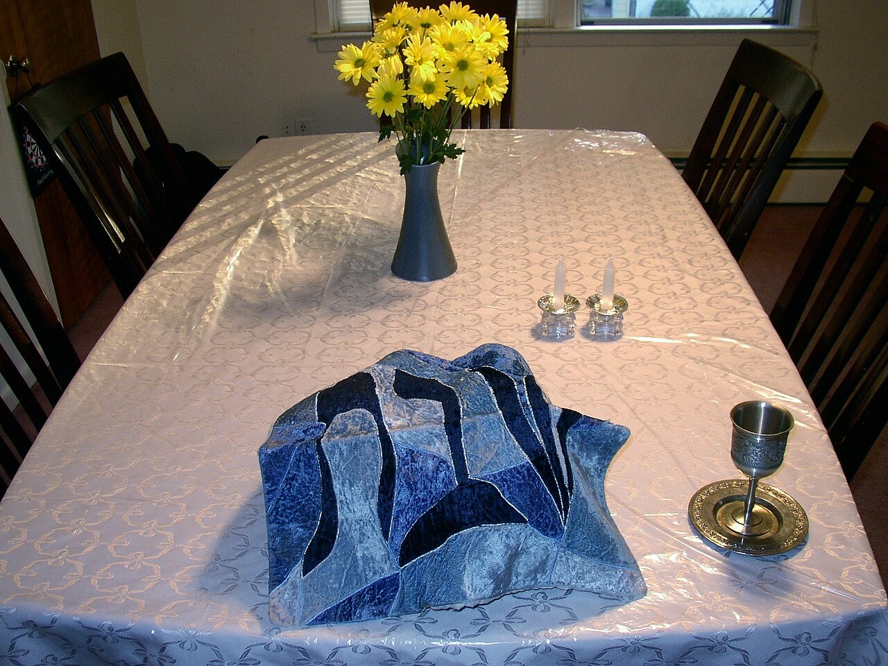 A Shabbat table set with candles, a covered challah, and a kiddush cup.