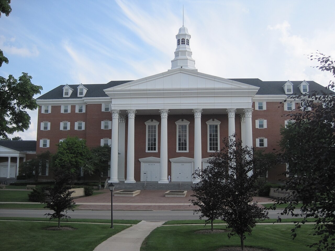 The Billy Graham Center at Wheaton College, a large brick building with a white columned portico and a small cupola, seen across a lawn.
