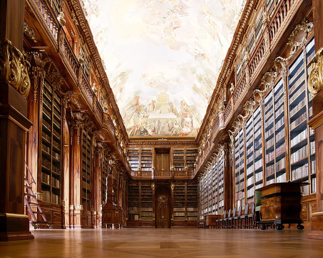 The Philosophical Hall of the Strahov Monastery library in Prague, a vaulted baroque reading room lined with tall bookcases beneath a painted ceiling.