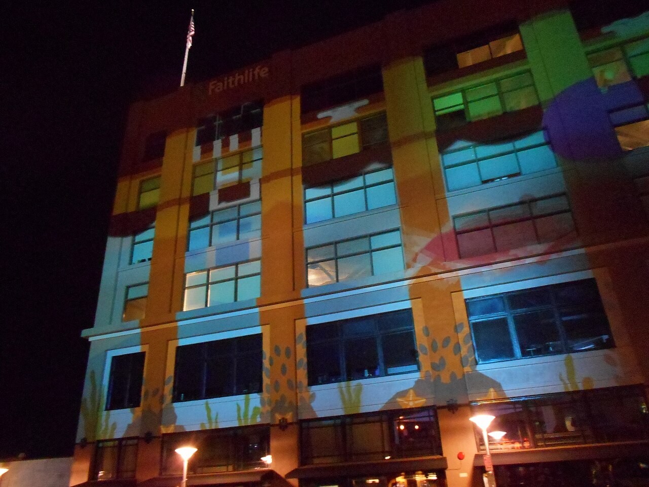 The Faithlife building in downtown Bellingham, Washington, at night, its facade washed in striped laser projections during an art walk, with the Faithlife name lit at the top.