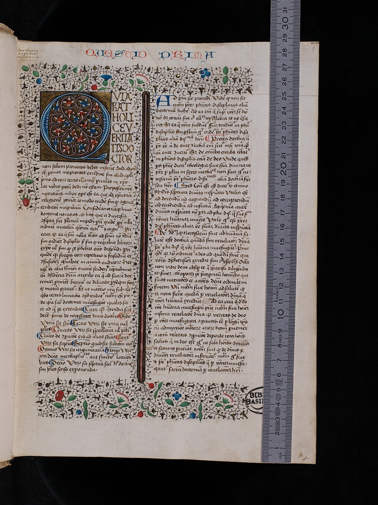 A manuscript page of Thomas Aquinas's Summa Theologiae, Latin text in two columns with a decorated initial and a floral border, photographed with a ruler at its edge.