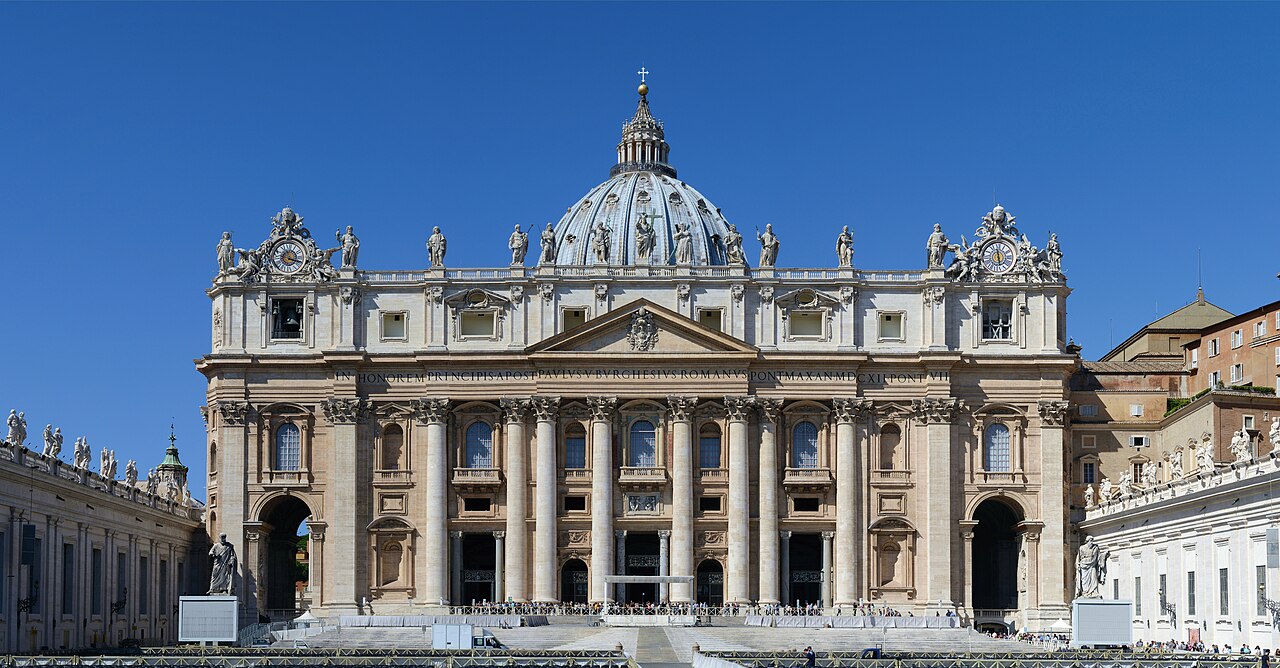 The facade and dome of St Peter's Basilica in Vatican City under a clear sky.