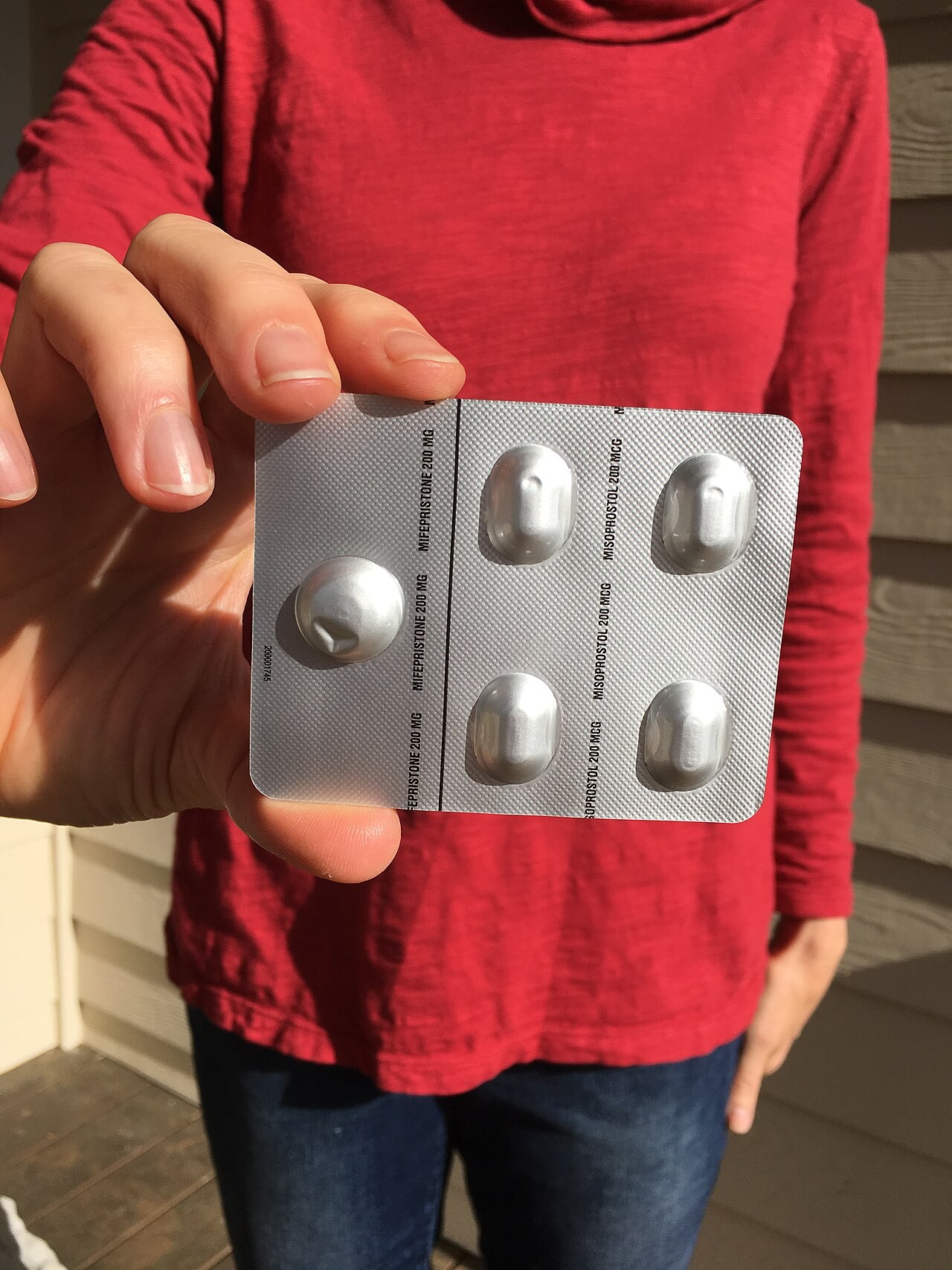 A hand holding up a blister card of four pills from a medical abortion kit.