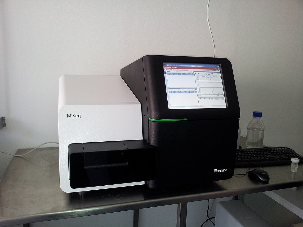 An Illumina MiSeq DNA sequencer on a laboratory bench, its screen lit.