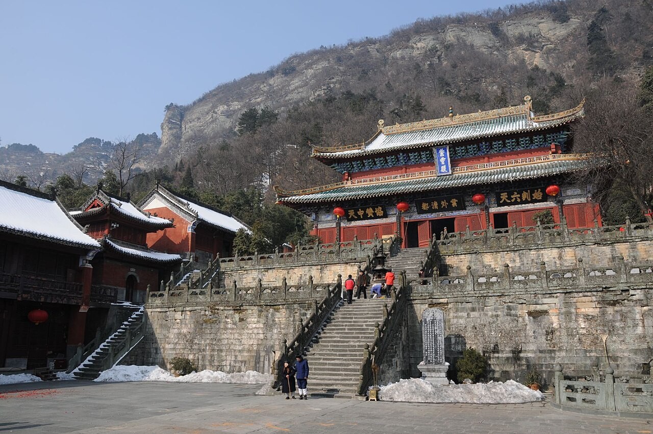 A temple hall of the Wudang Mountains, red walls and tiled roofs above a stone terrace in the snow.