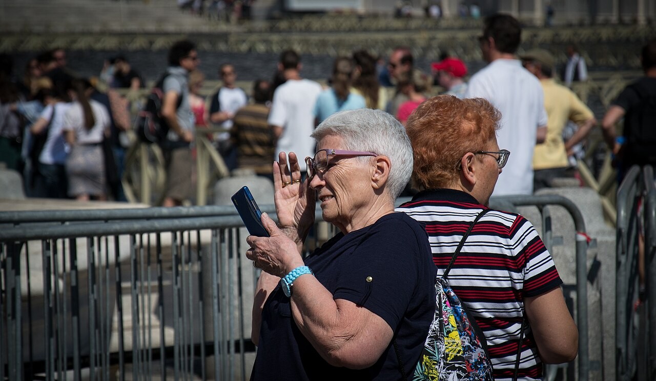 A street crowd in which a woman in the foreground holds a smartphone up before her face.