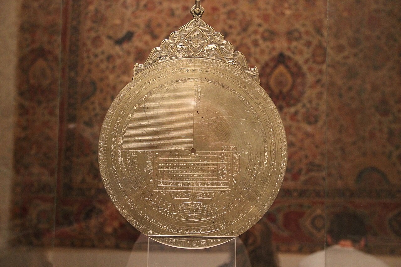 A large brass Islamic astrolabe on display, its engraved plates and rete photographed face-on.