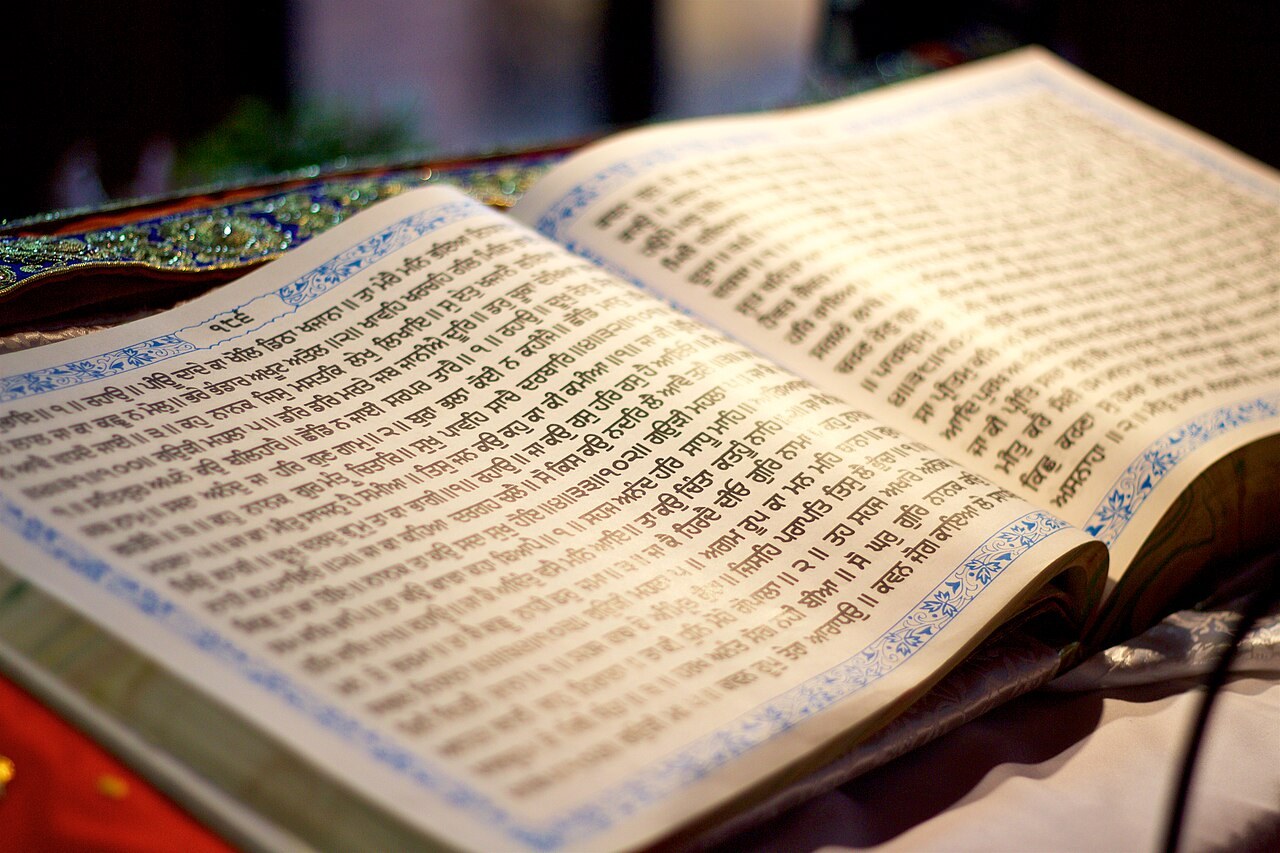 An open copy of the Guru Granth Sahib, its pages filled with hymns written in the Gurmukhi script.
