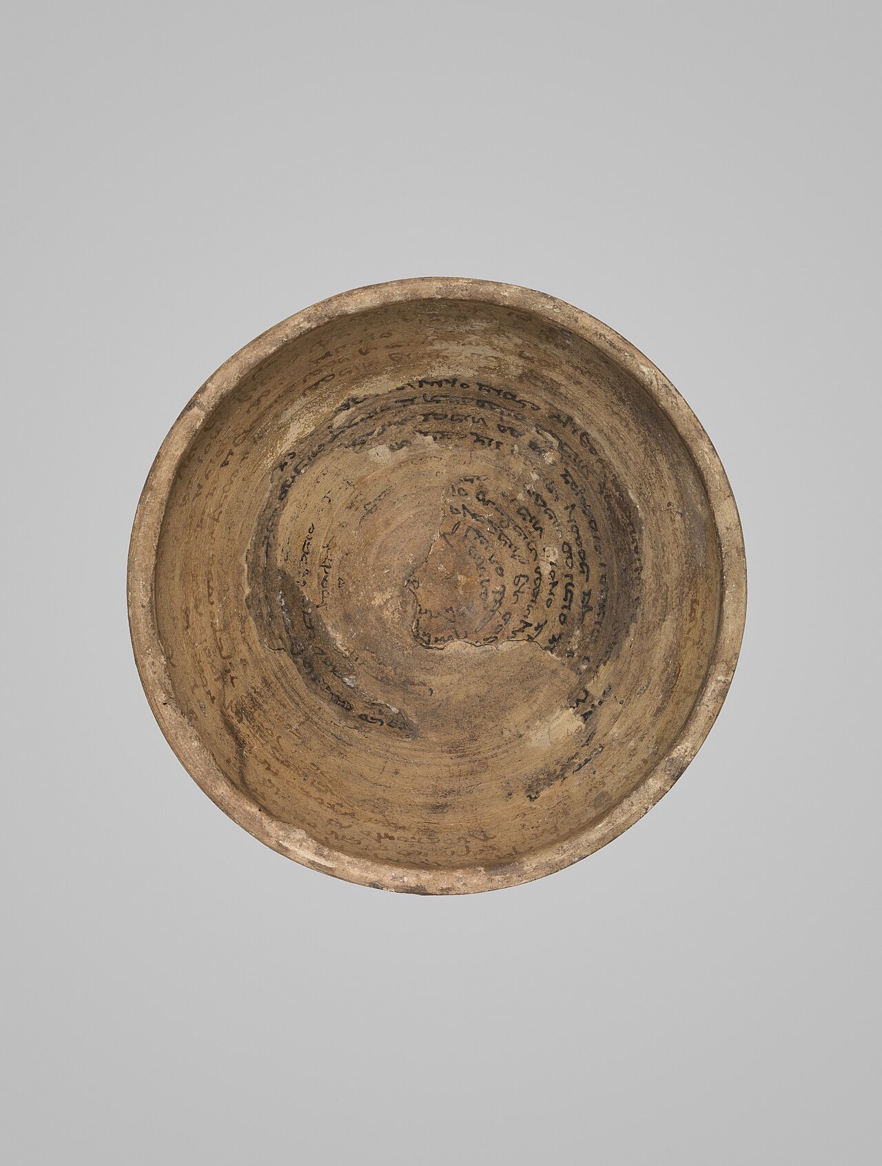 A clay incantation bowl whose inside is covered with a spiral of handwritten Mandaic script.