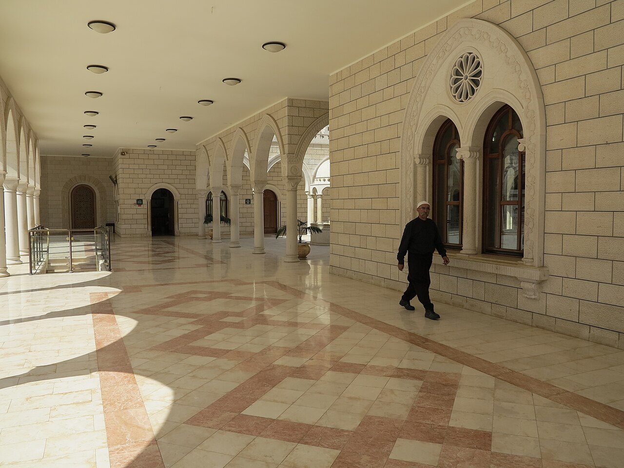 The sunlit stone courtyard of the Nabi Shu'ayb shrine, the Druze holy site near Hittin, with arched colonnades and a patterned marble floor.