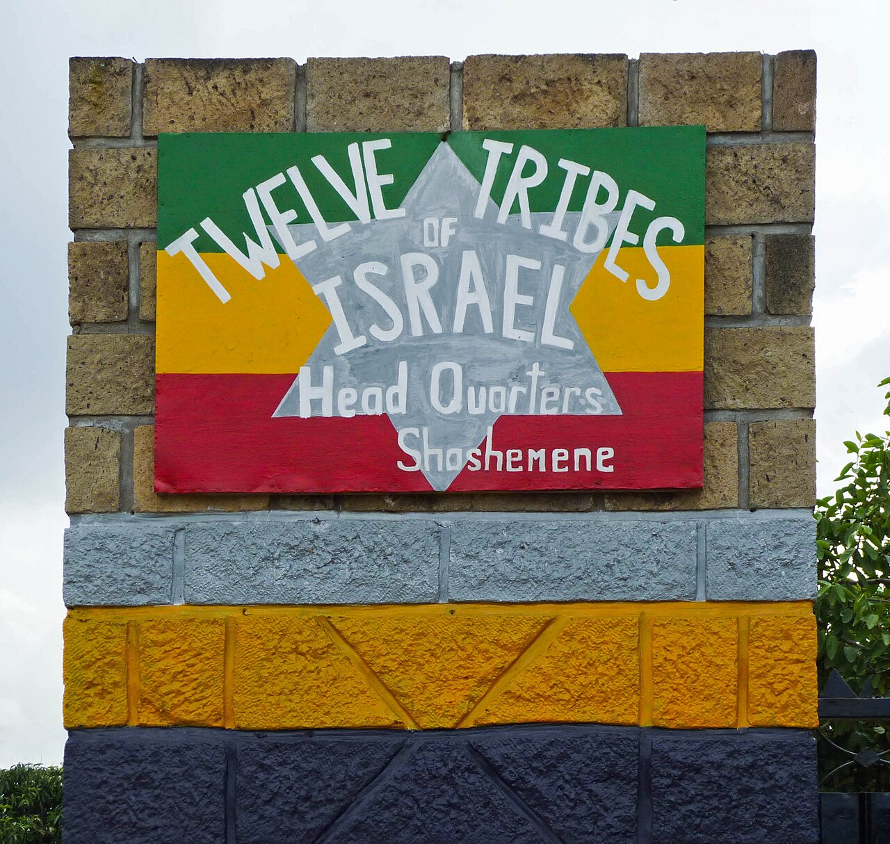 A painted sign on a brick gate pillar reads Twelve Tribes of Israel Head Quarters Shashemene, with a silver Star of David over green, gold, and red stripes, at the Rastafari settlement in Ethiopia.