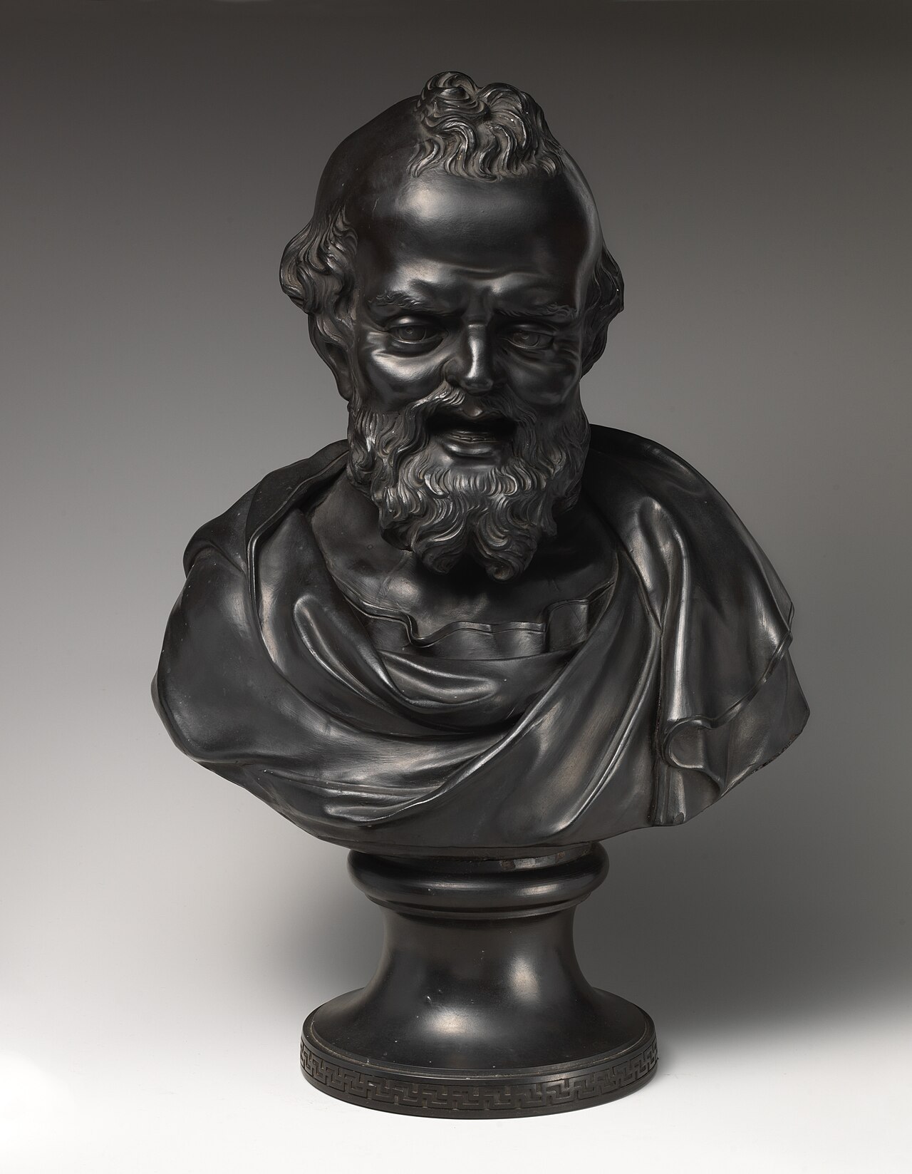A glossy black stoneware bust of the laughing Democritus, bearded and draped, grinning on a round pedestal.