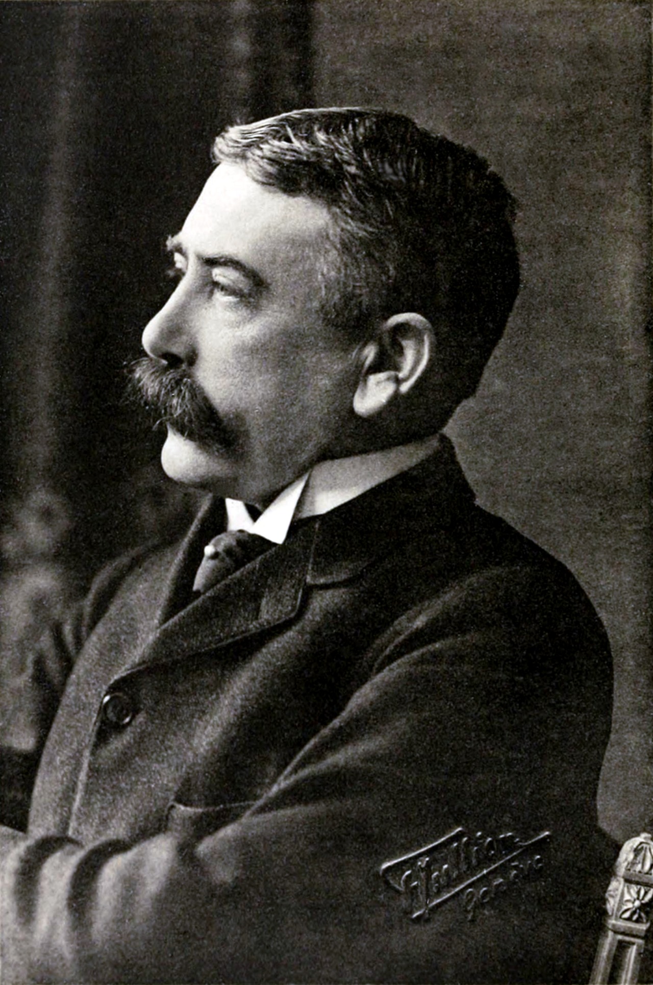 A black-and-white studio photograph of Ferdinand de Saussure in left profile, a mustached man in a dark suit, the Jullien Genève studio mark visible.