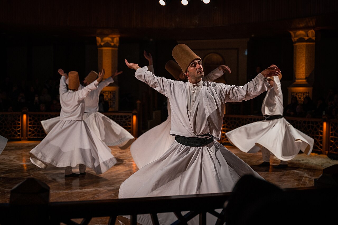 Mevlevi dervishes in white robes and tall felt hats turning in the sema ceremony.