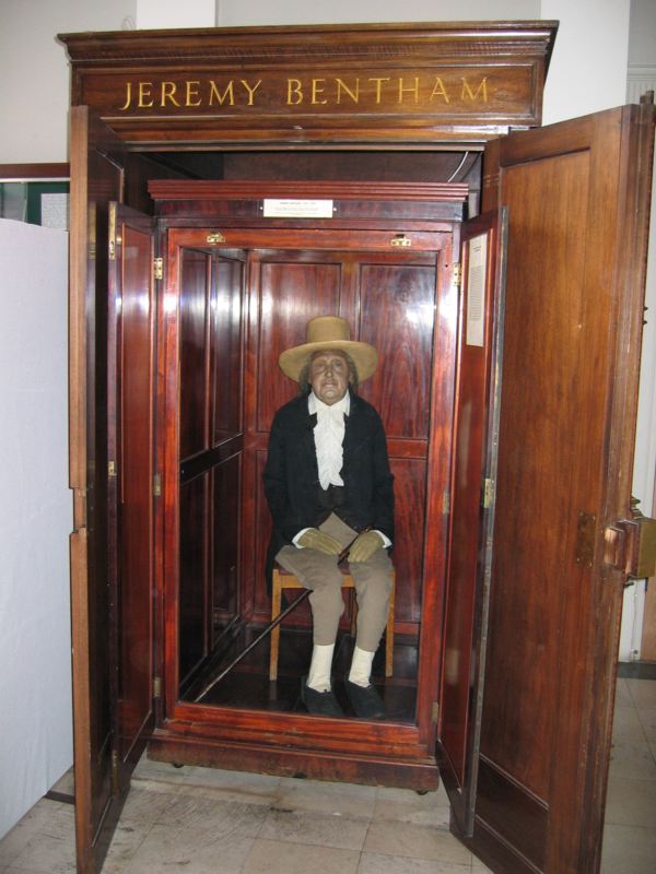 Jeremy Bentham's auto-icon: his dressed figure with wax head, cane, and broad-brimmed hat, seated inside its open wooden cabinet at University College London.
